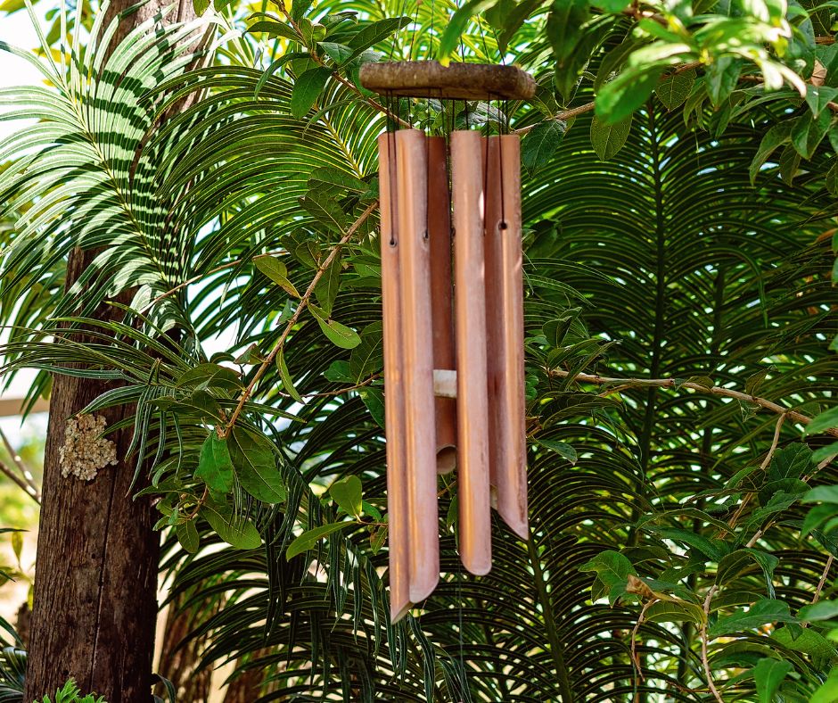 Rustic brass and wood wind chimes in a lush garden.