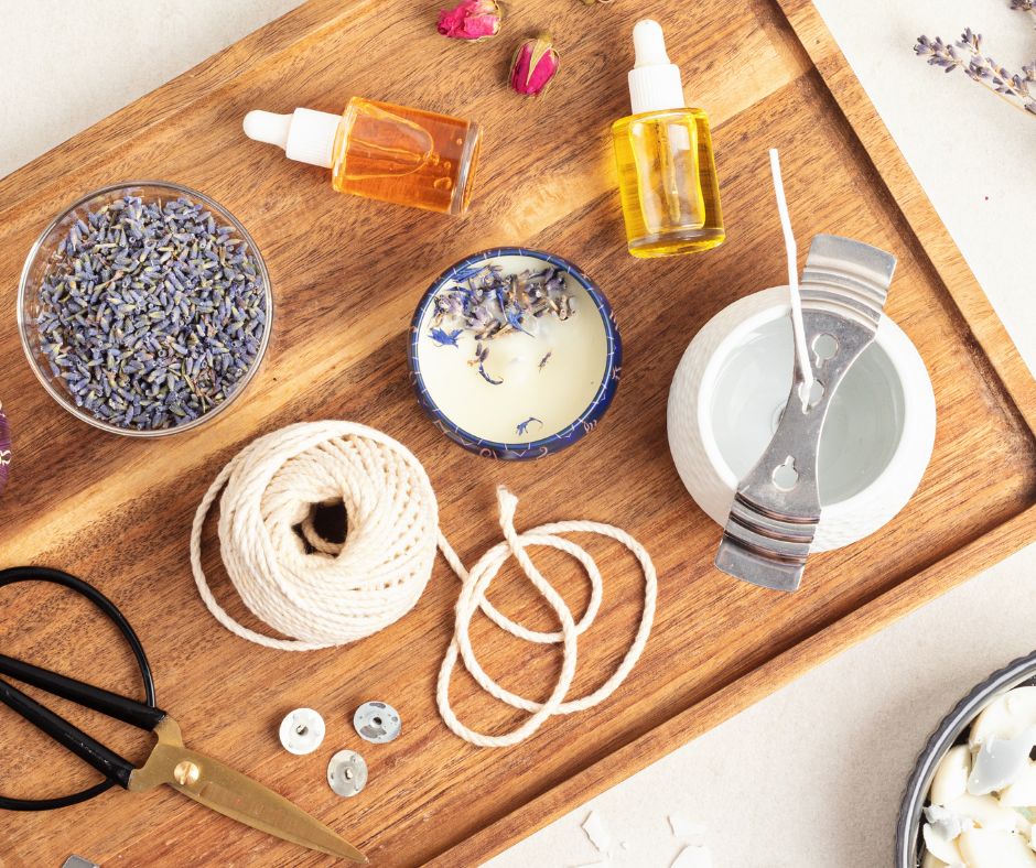A wooden tray with candle making supplies on it. Including, wick, wax, containers and essential oils.