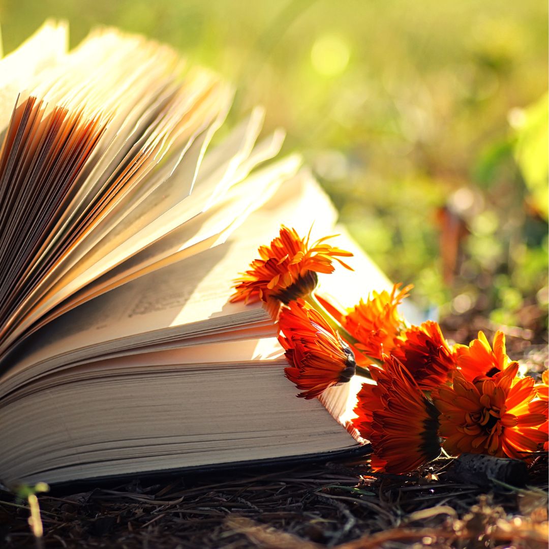 An open book lying on the ground next to a bouquet of calendula flowers.