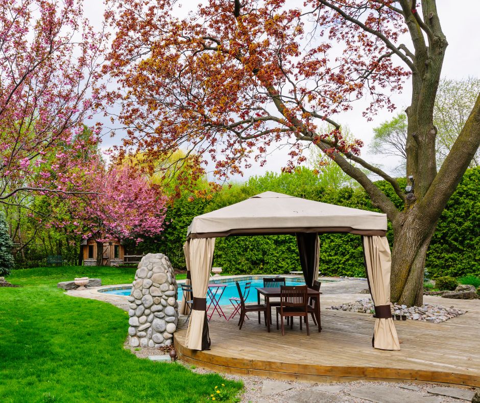 A beige canvas gazebo with curtains next to a pool.