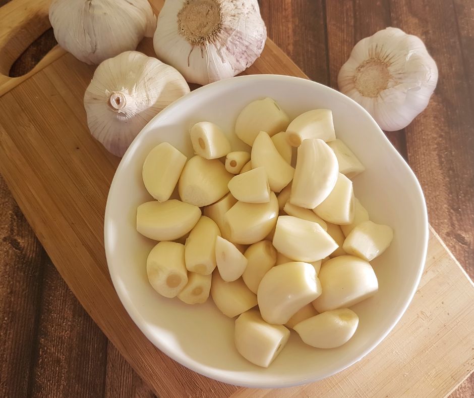 Whole garlic bulbs and peeled garlic cloves in a kitchen on a wooden table.
