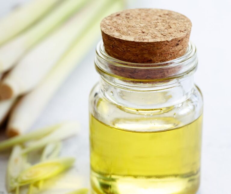Lemongrass oil in a glass jar with a cork top next to a bunch of cut lemongrass.