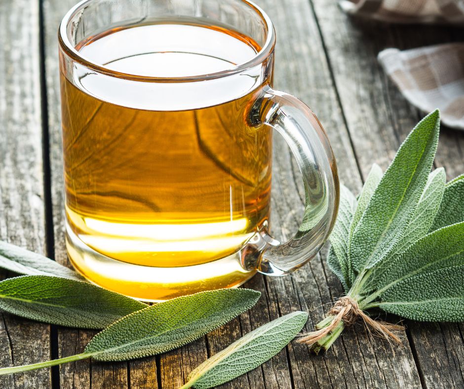 Sage tea in a clear mug next to fresh sage sprigs.