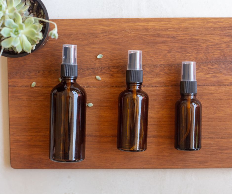 Amber spray bottles in three different sizes on wooden table.
