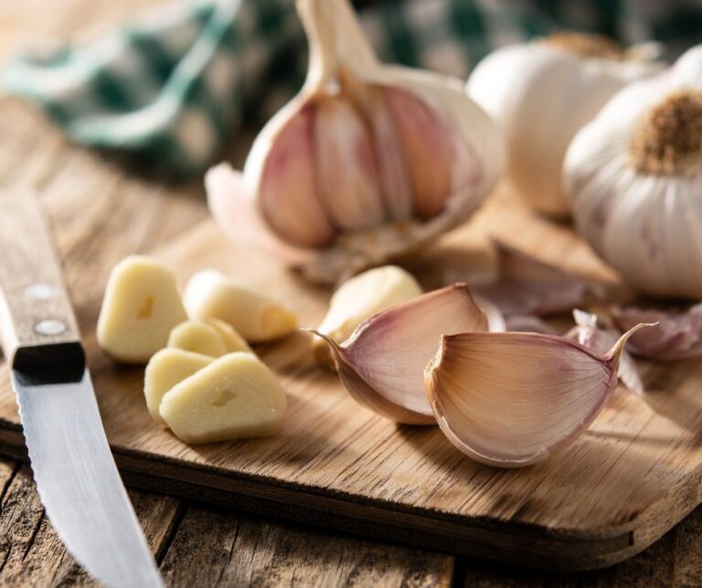 Garlic cloves and bulbs on a wooden table with knife.