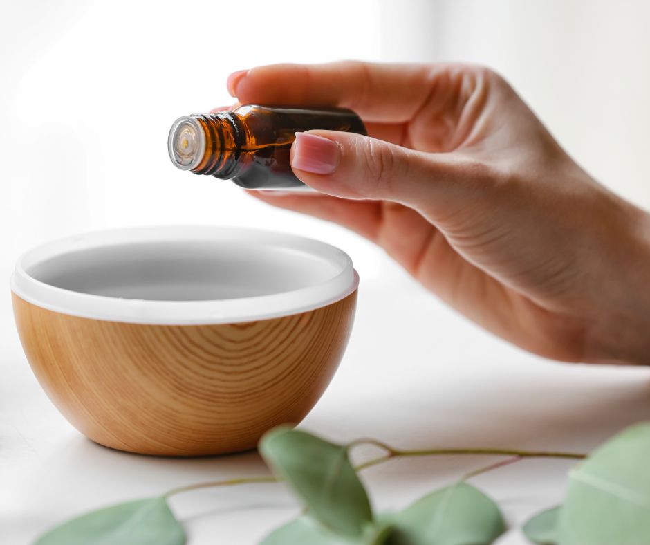 A hand pouring essential oil into a white and wood bowl.