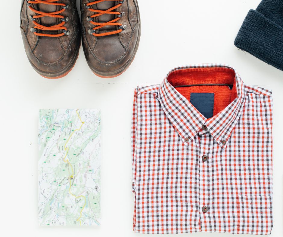 An assortment of outdoor gear. Including a map, plaid shirt, hiking boots and a knit cap.