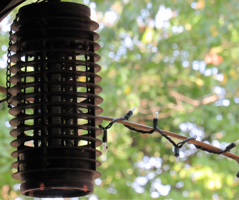 A black bug zapper hanging on a patio near string lights.