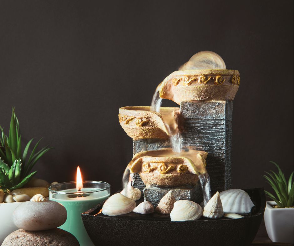 A small cascading table top water fountain next to a lit candle.