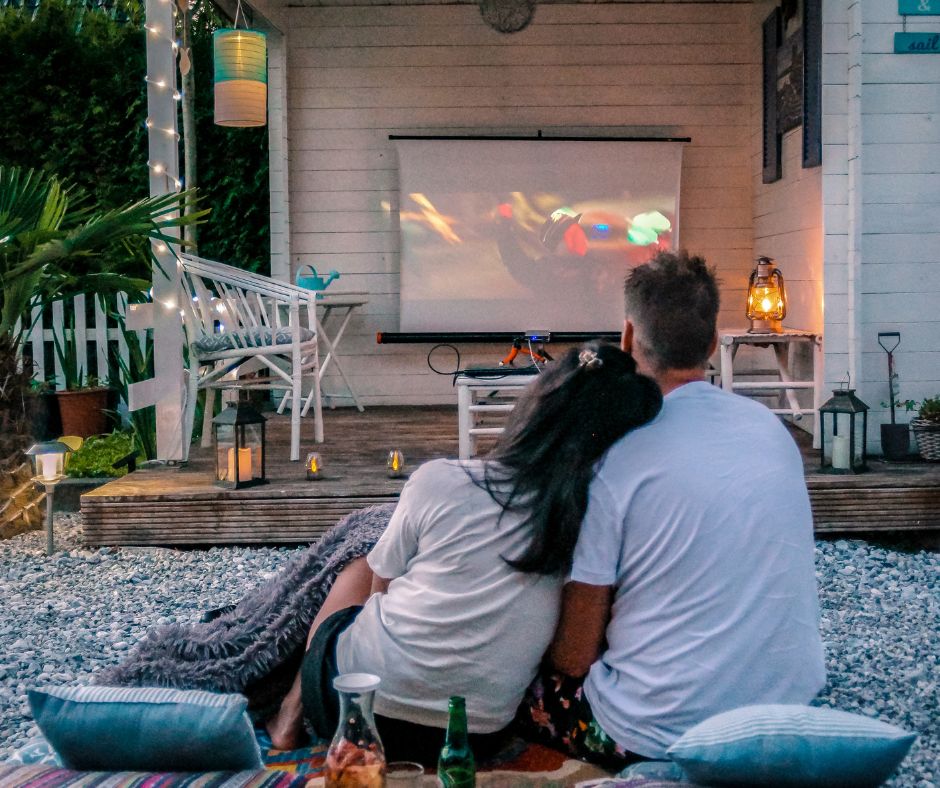 A couple sitting in the garden watching a movie on an screen.