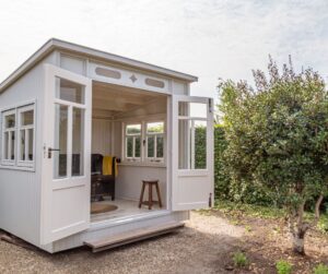 A high end studio shed in a garden next to a fruit tree.