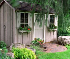 A wooden garden shed with windows and flower boxes.