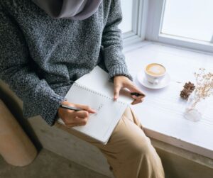 A person sitting at a window journaling.