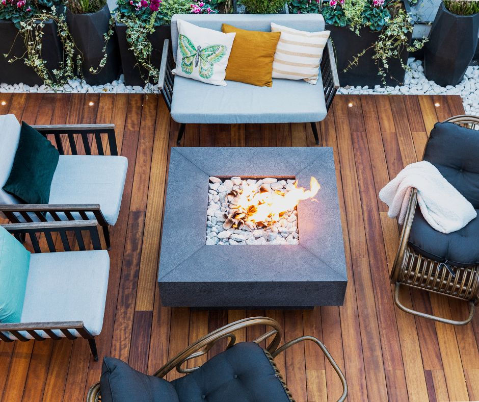 A cozy deck seating surrounding a gas fire pit.