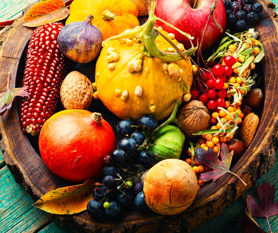 A basket full of fall produce. Including squash, grapes, corn, figs and pomegranates.