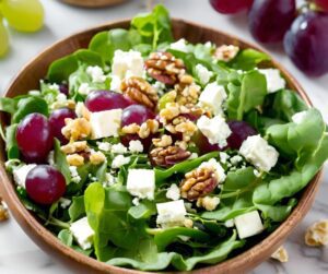 A large salad of greens, grapes, feta and walnuts in a wooden bowl.