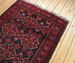 A red and black rug on a wooden deck.