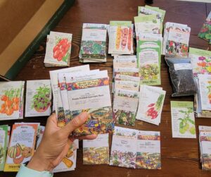An assortment of seed packets on a table. A hand holding four.