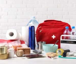 A grouping of common emergency supplies including food, water, a first aid kit, and a radio.