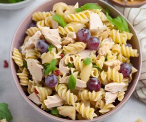 A large bowl of chicken pasta salad containing grapes, cheese and fresh herbs.