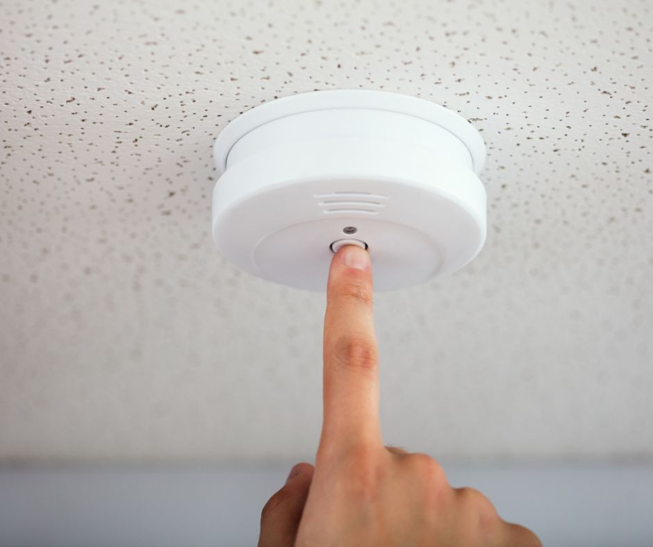 A hand pressing a smoke detector button.