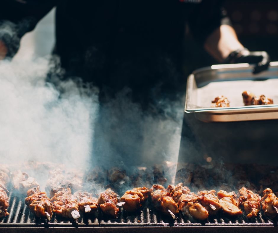 A person grilling a large number of meat on skewers in a backyard.