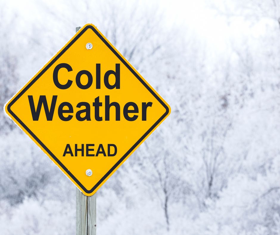 A yellow caution sign in a winter landscape with the words " cold weather ahead" in black letters.