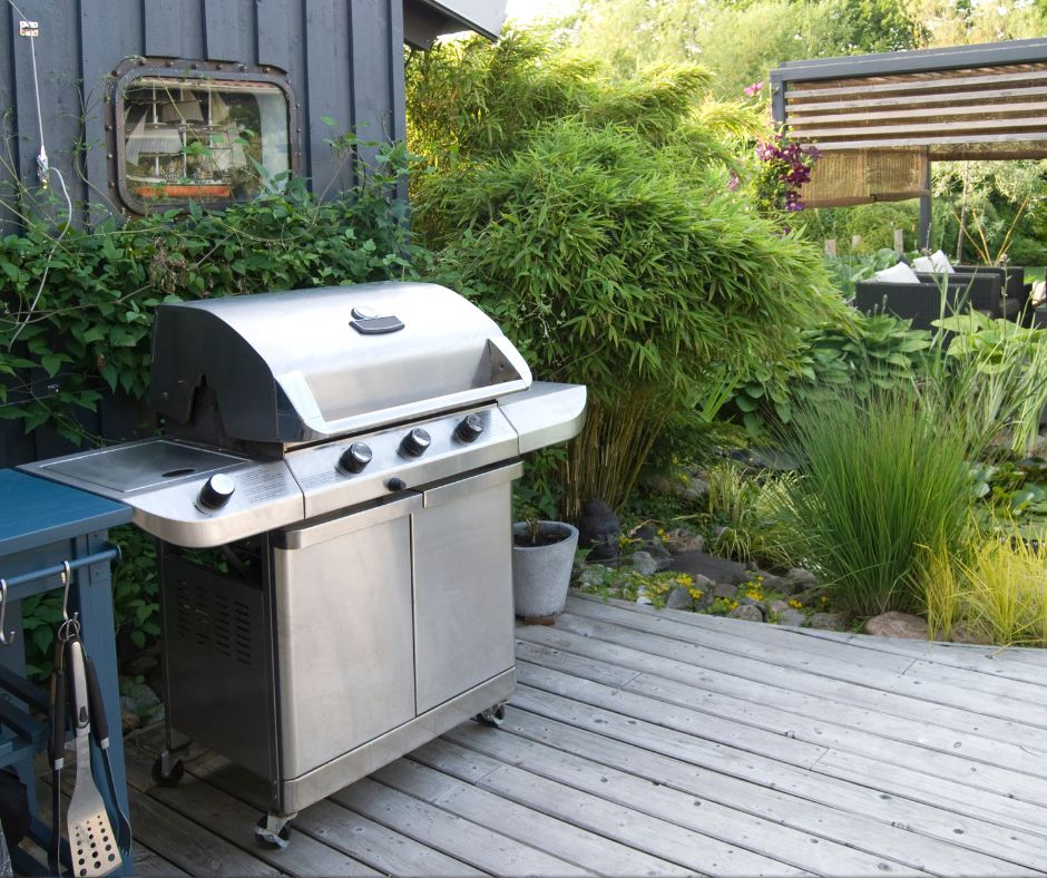 A gas grill in a private backyard on a deck next to a pond.