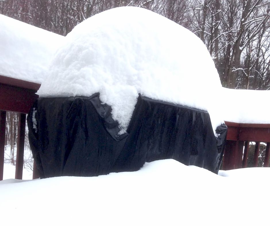 A covered grill with snow on it.