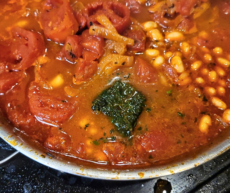 A cube of frozen basil and olive oil melting into a pan on tomato and white beans.