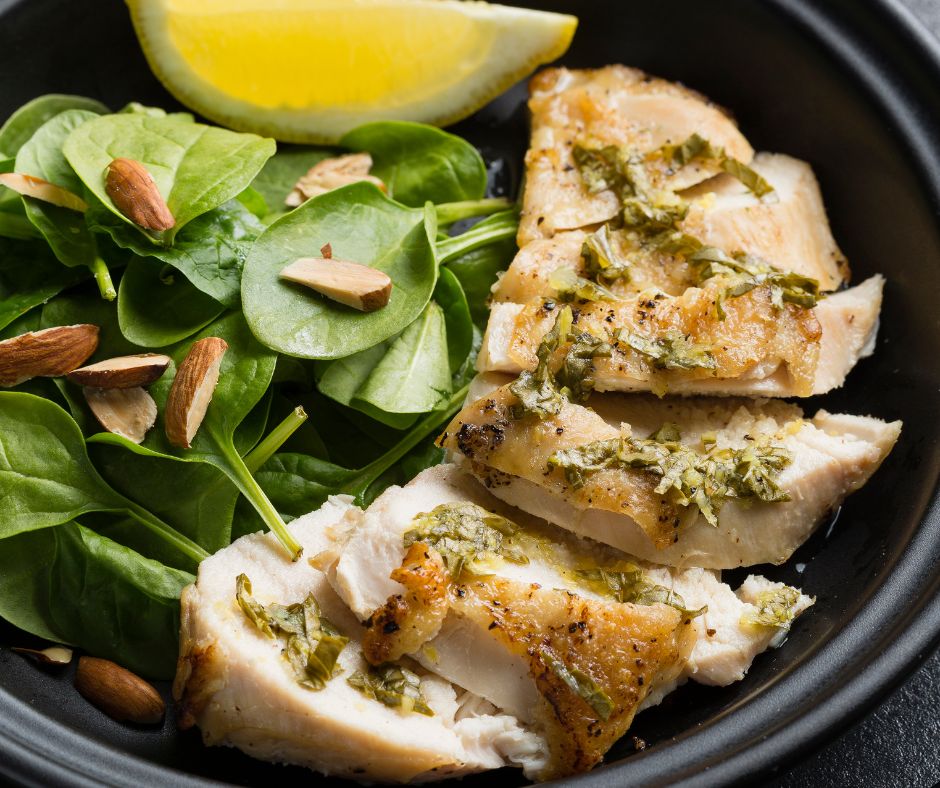 Sliced lemon basil chicken breast on a plate next to a simple spinach salad.