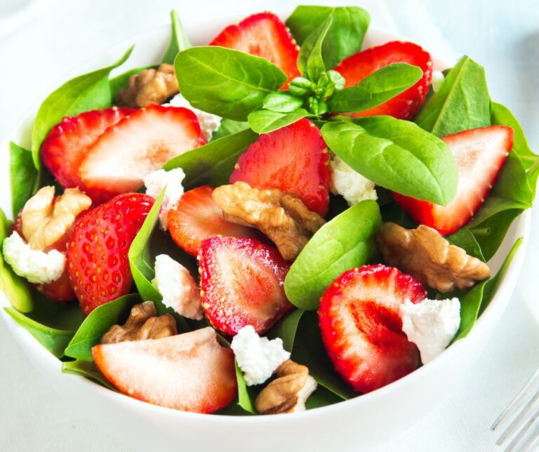 A bright salad with red strawberries, fetta cheese cubes, walnuts and green basil leaves.