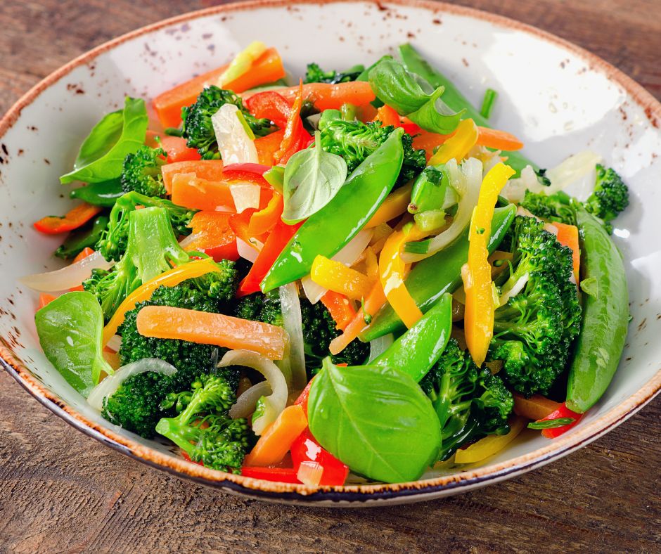 A mix of stir fired veggies and basil in an earthen bowl.