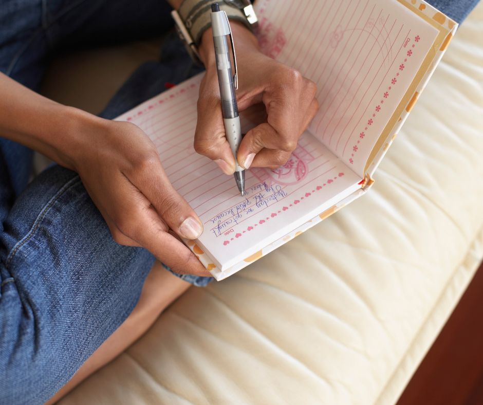 A person journaling on a white couch.