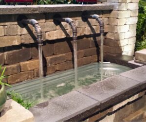 A fountain with multiple pipes pouring rainwater into a basin.