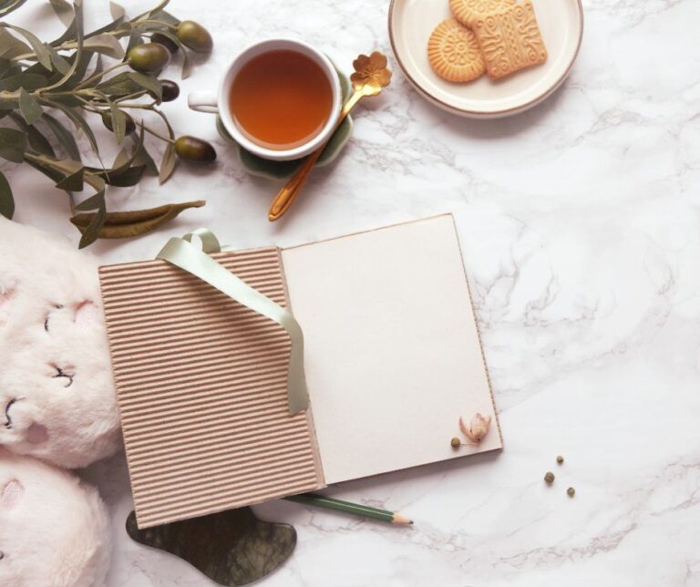 An open journal next to tea, biscuits, and flowers.