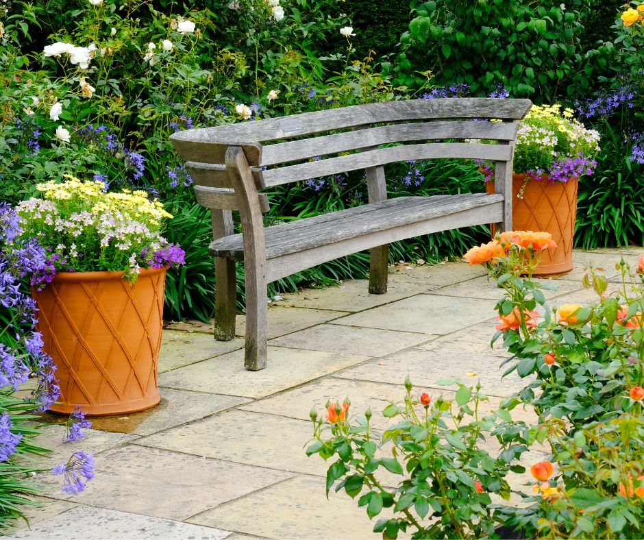 A curved garden bench on a garden path next to potted flowers.