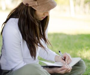 A person sitting in grass on a summer day journaling.