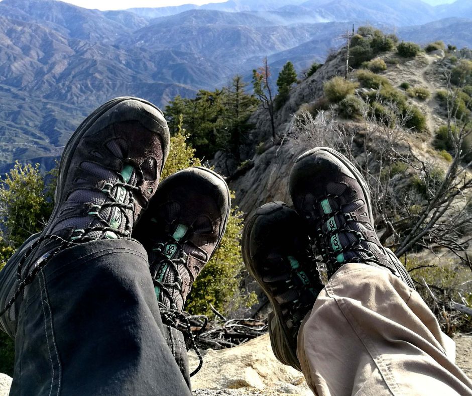 Two hikers resting their feet at a mountain overlook.