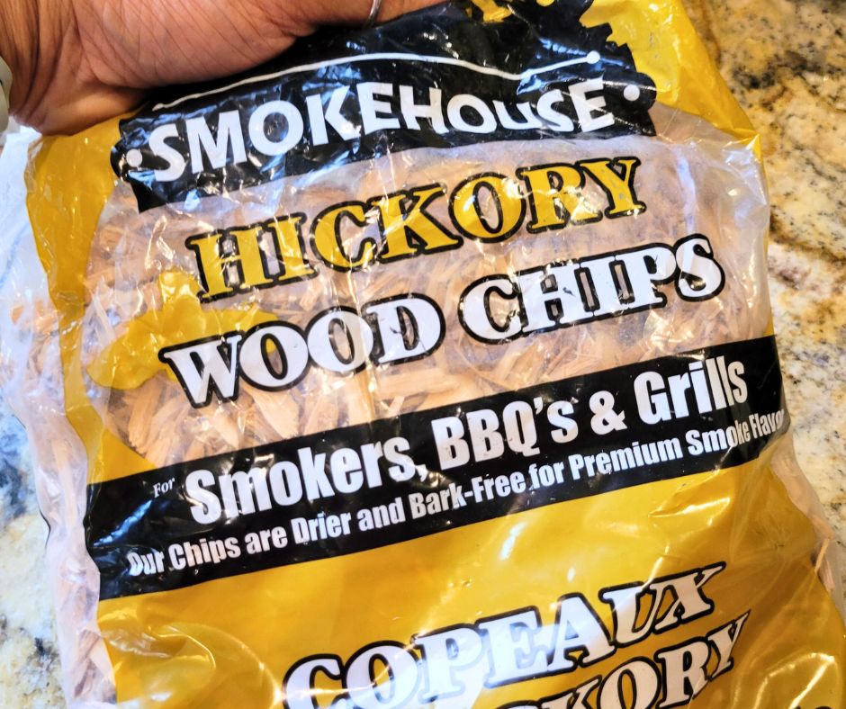 A person holding a bag of wood chips labeled "Hickory."