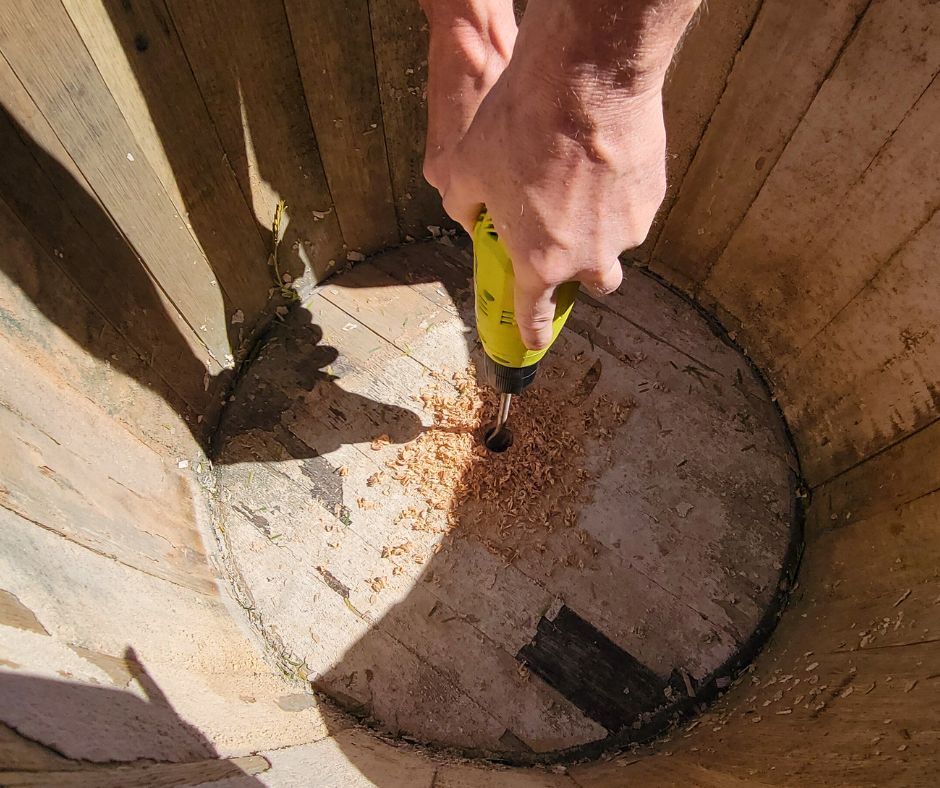 A person drilling a hole into the bottom of a wooden planter.