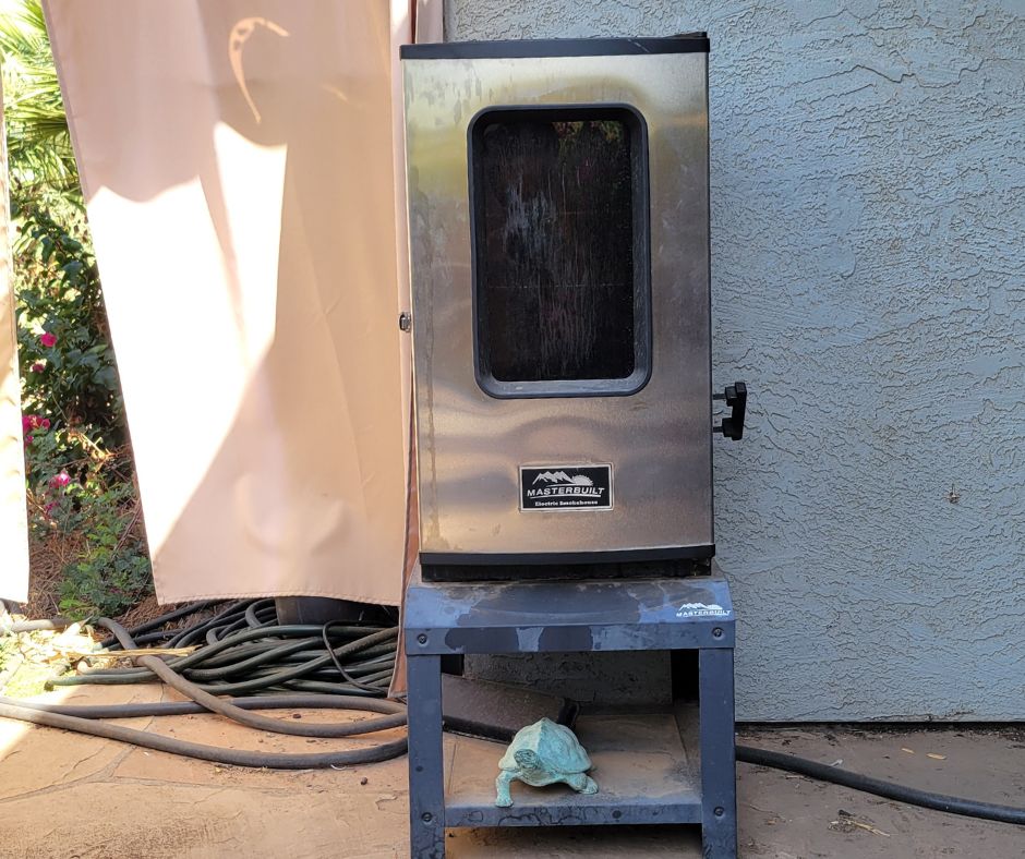 Stainless steel Masterbuilt electric smoker on a patio with outdoor curtains.
