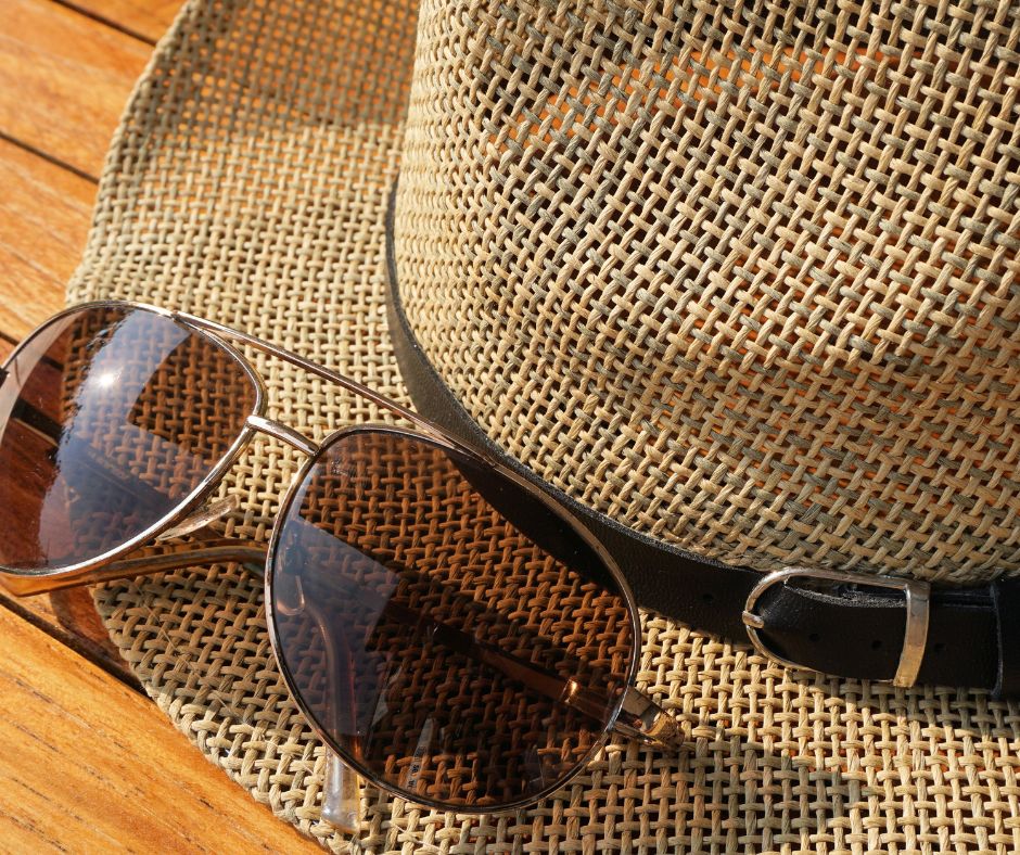 A straw hat and sunglasses on a wooden table.