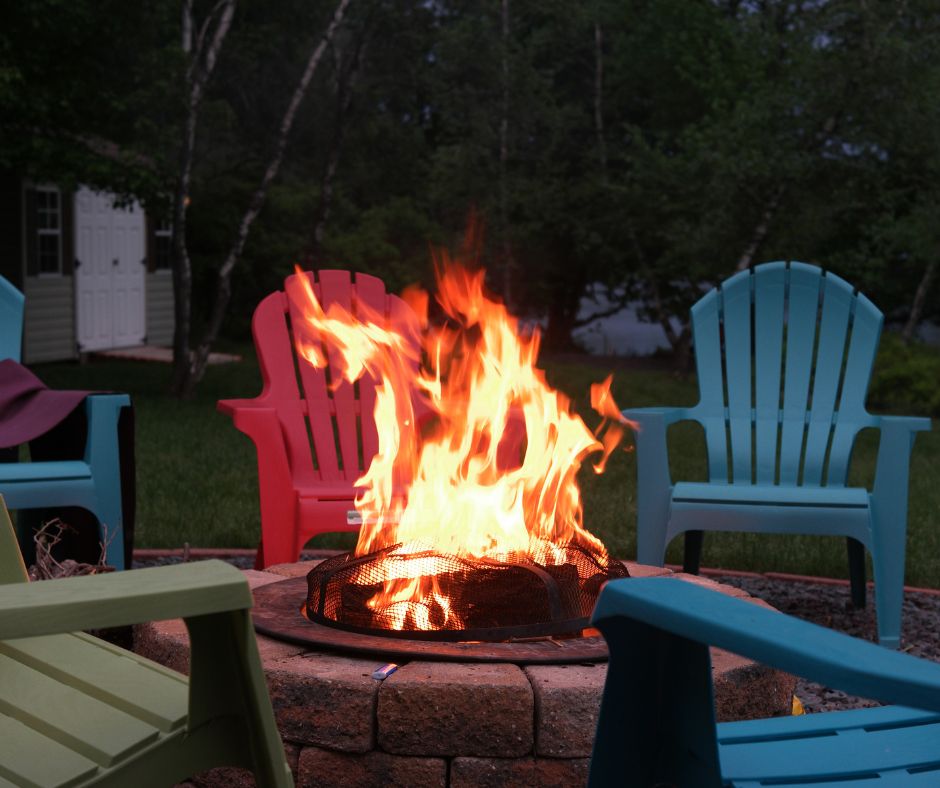 A fire burning in a fire pit surrounded by colorful chairs.