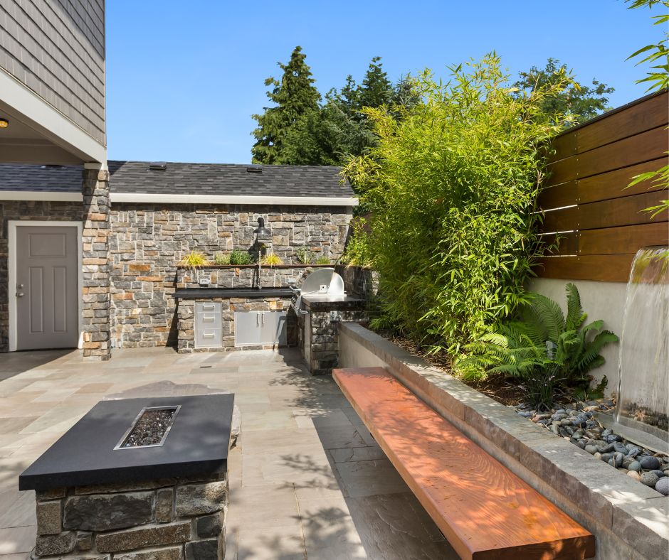 A stone patio with an outdoor kitchen, fire pit, and seating area backed by a relaxing water feature.