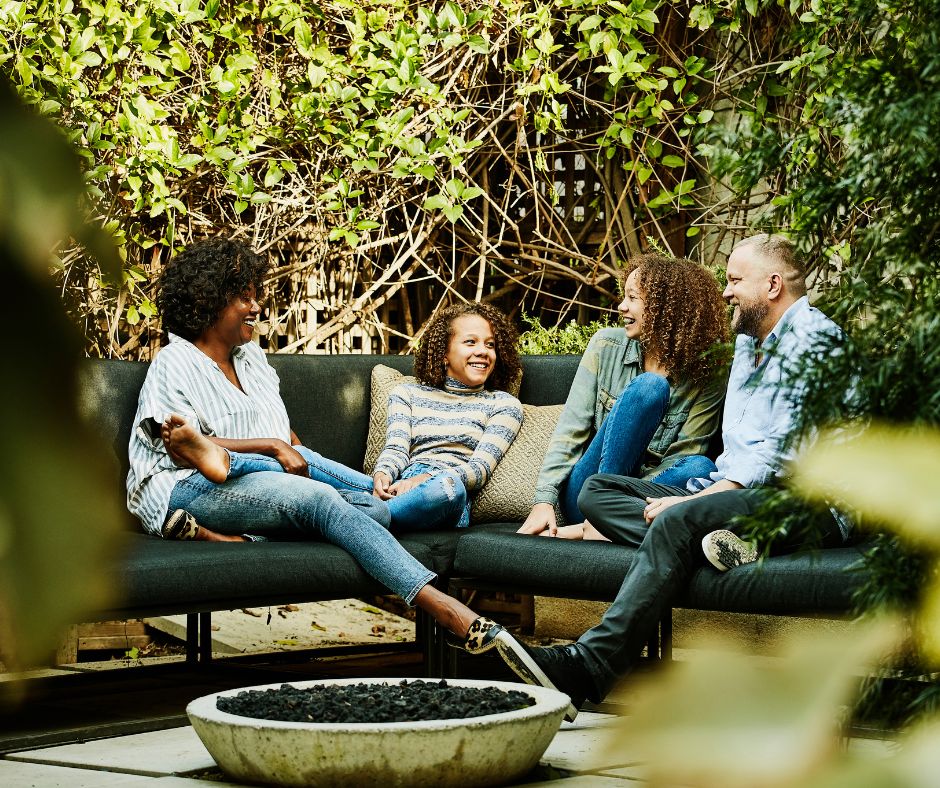 A Family chatting in an outdoor living room featuring a fire pit and lush privacy screens.