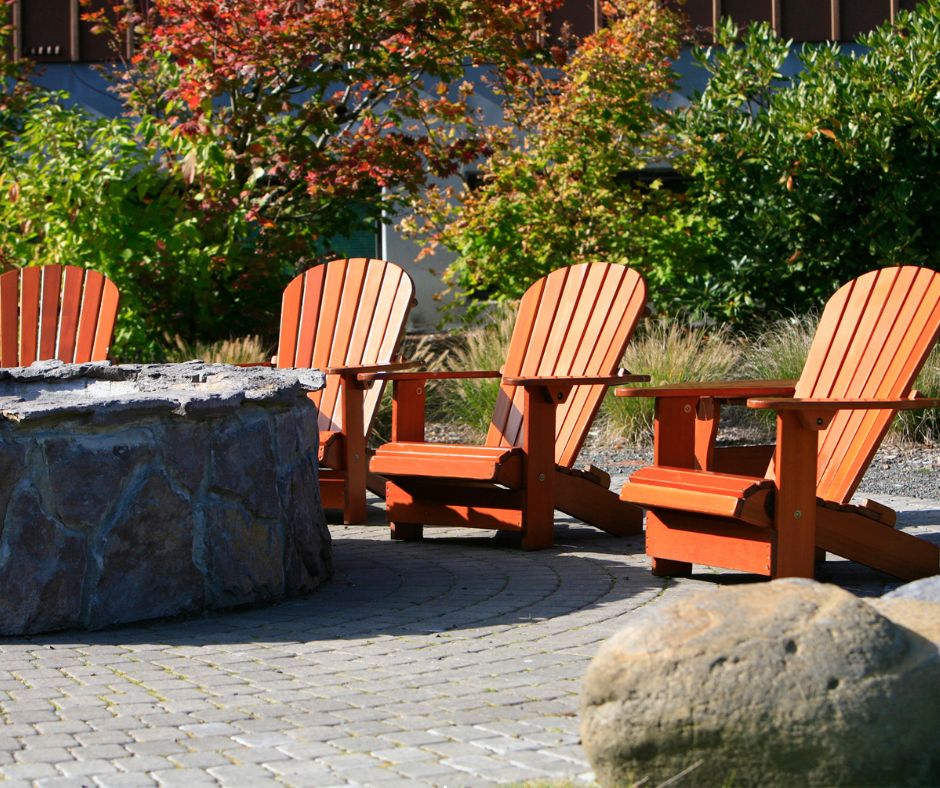 High back chairs next to a stone fire pit surrounded by fall foliage.