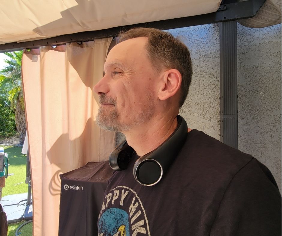 A man enjoying his portable neck fan on a patio.