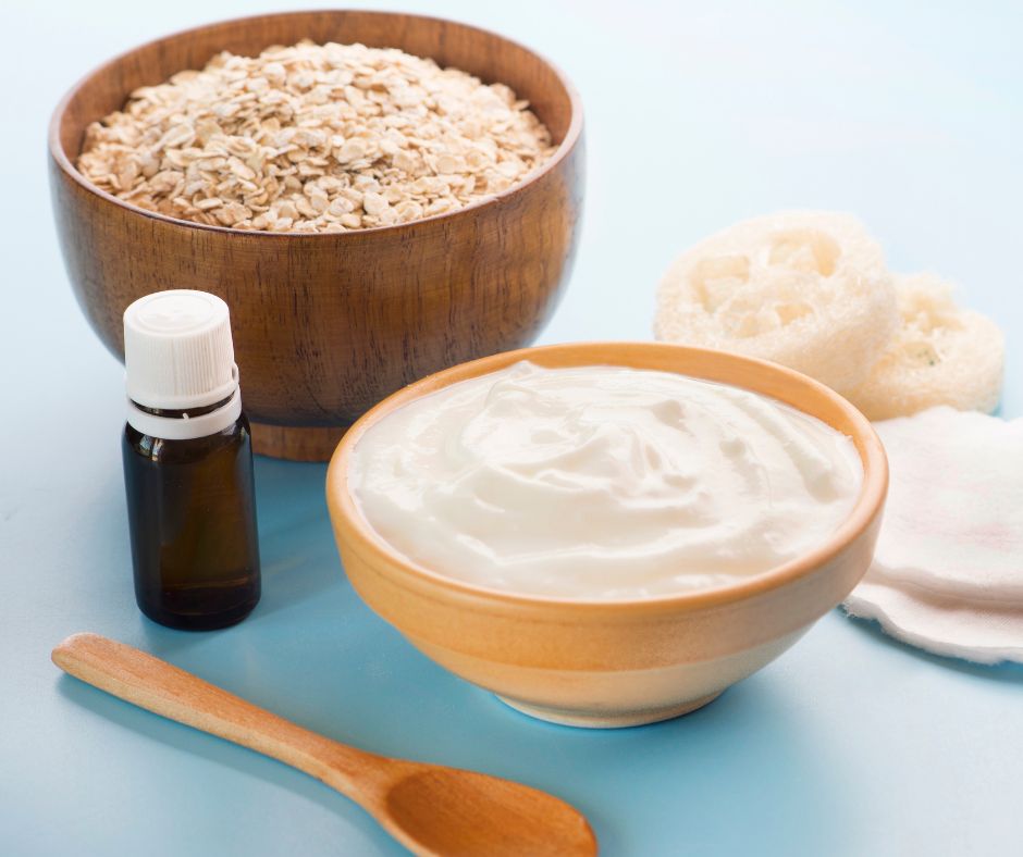 Bowls of oats and yogurt on a table with an essential oil bottle and natural sponges.
