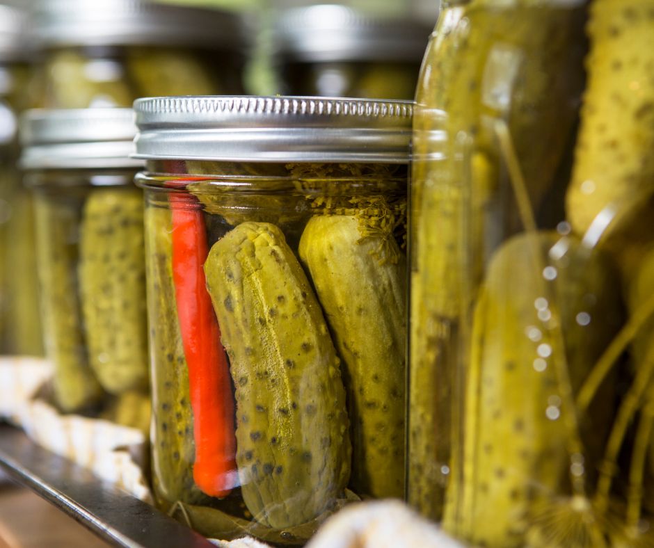 A shelf of home canned pickles with different herb and spice mixes. Including whole red chili and dill.